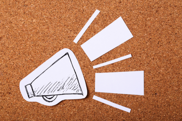 A cutout of a handdrawn megaphone pinned to a corkboard